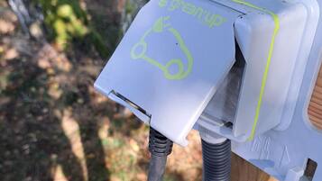 A close-up of a white electrical box with a green logo, attached to a wooden post with a black cable connected to it.