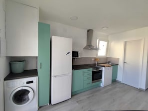 A compact kitchen with a washing machine, a refrigerator, a microwave, and a stove.