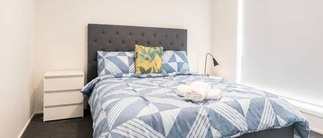 A bedroom with a bed, a nightstand, a lamp, and a window.