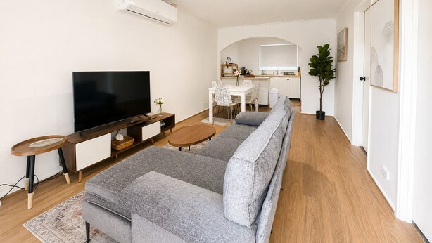 Een moderne woonkamer met een bank, televisie en een eethoek, met een keuken op de achtergrond.
