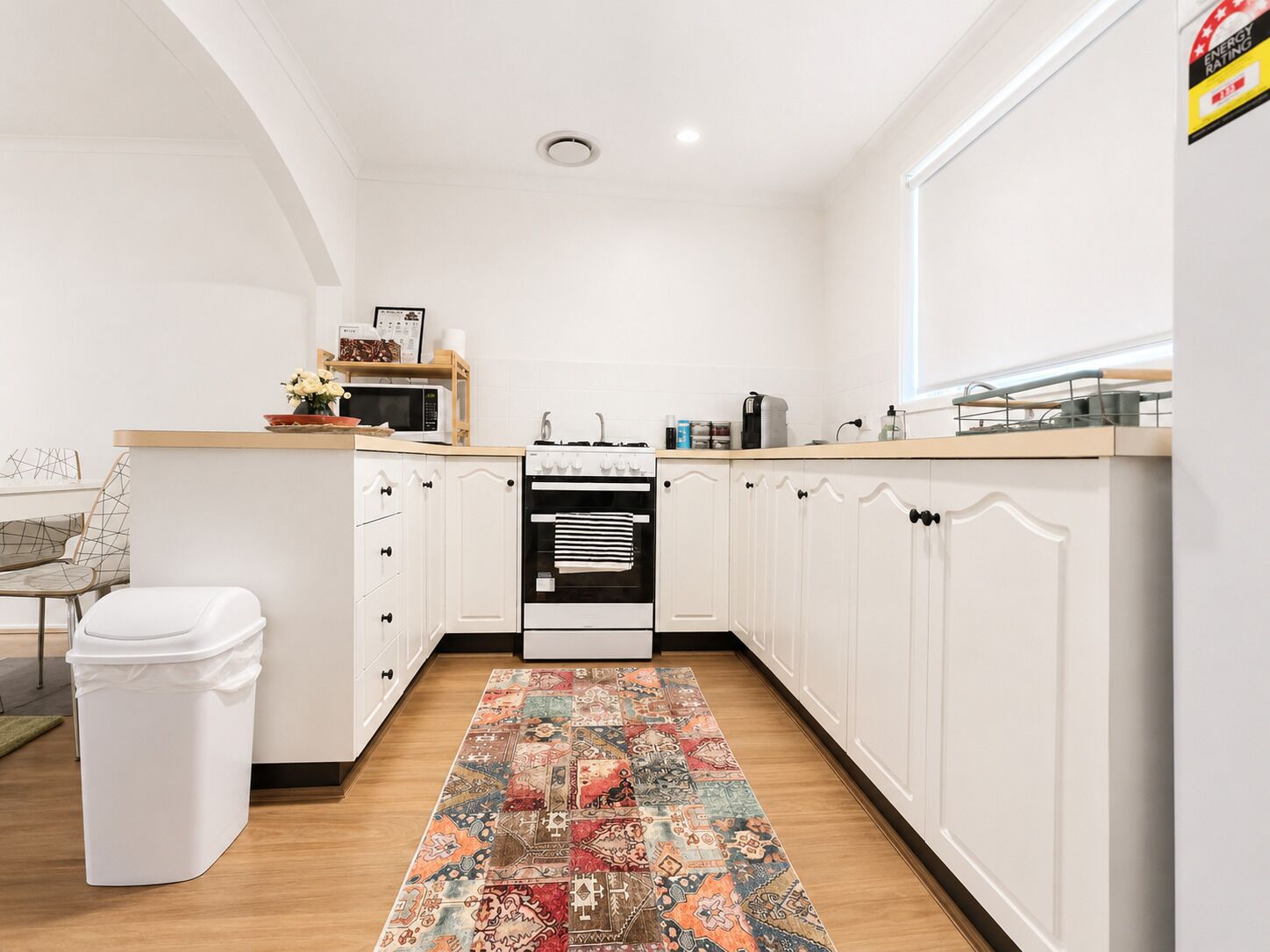 A modern kitchen with white cabinetry, a microwave, stove, and a patterned rug.