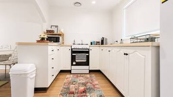 A modern kitchen with white cabinetry, a microwave, stove, and a patterned rug.
