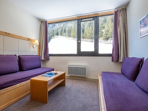 Et værelse med en seng, sofa, et lille bord, et vindue med gardiner og en radiator.