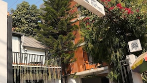 An entrance to a building with a sign reading 'SAMS APARTMENT,' a covered outdoor seating area, and a potted plant. - Sam's Apartment (Lalitpur)