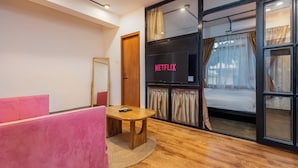 A modern room with a wooden floor, a round table, a pink couch, and a large window with curtains. - Sam's Apartment (Lalitpur)