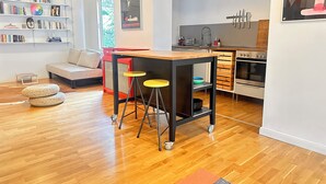 Een moderne keuken met een ingebouwde oven, een eethoek met krukken en een boekenplank vol boeken.