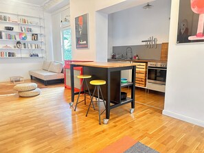 A modern kitchen with a built-in oven, a dining area with stools, and a bookshelf filled with books. - Central apartment, 4 beds, fully equipped kitchen, free parking spaces (Berlin)
