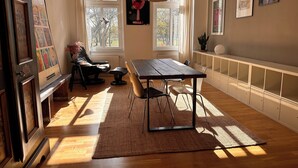 Een kamer met een houten tafel, stoelen, een vloerkleed, een radiator en kunst aan de wanden.