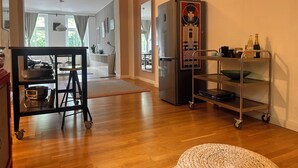 Een moderne keuken met een roestvrijstalen koelkast, een karretje met keukengerei en een geweven poef.