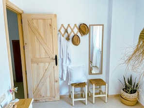 Eine Holztür, zwei weiße Hocker, ein Spiegel und ein Blumentopf in einer Ecke.