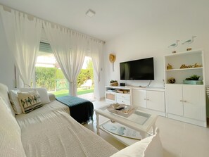Ein Wohnzimmer mit Sofa, Couchtisch, Fernseher und Blick auf einen Garten.