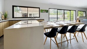 Cocina moderna con una isla grande, comedor con sillas y ventanas amplias que ofrecen vistas al exterior.