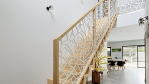 Una escalera moderna con barandilla geométrica, escalones de madera y una zona de comedor con sillas y una mesa.
