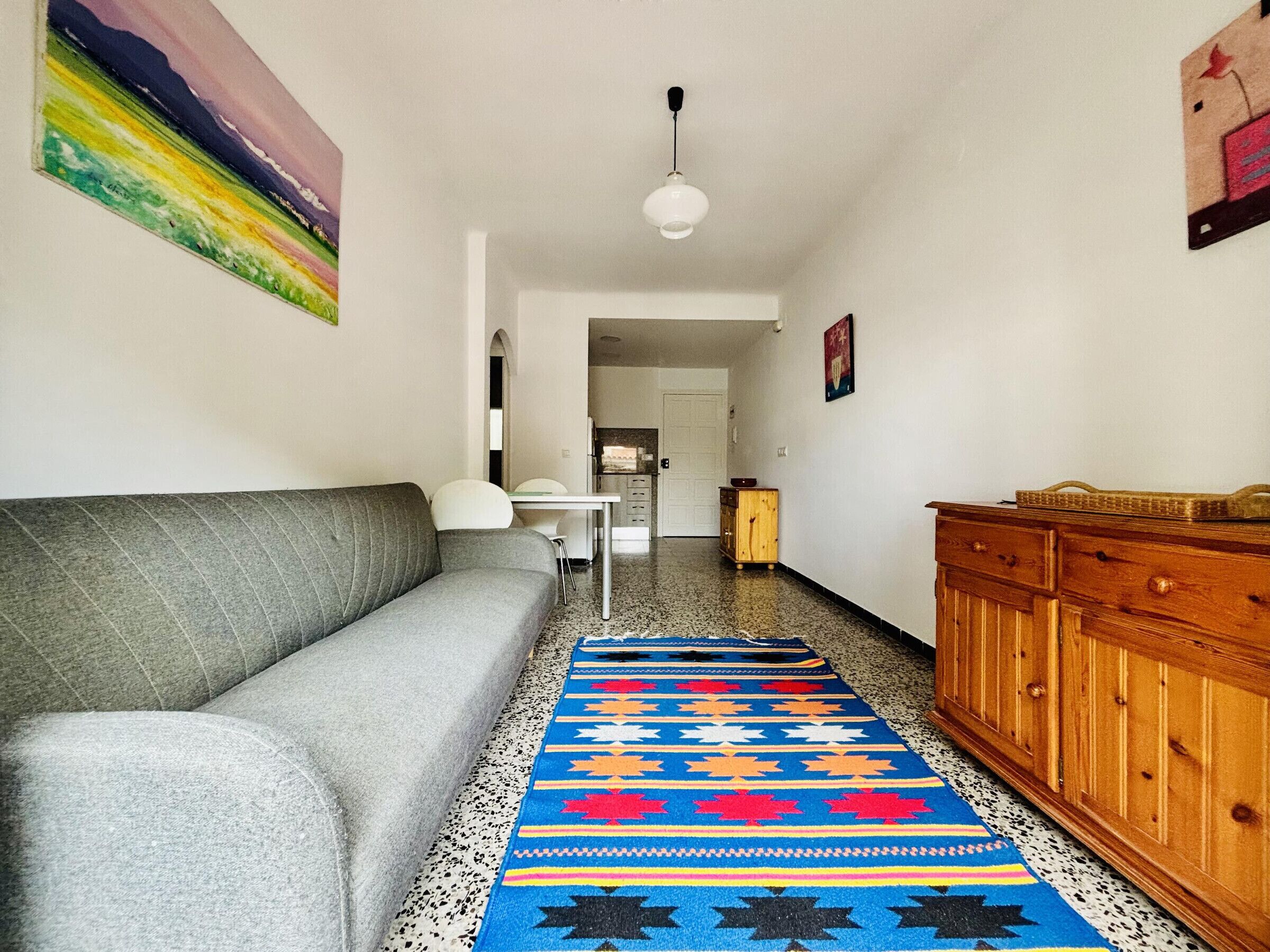 A hallway with a grey sofa, a wooden cabinet, a patterned rug, and a painting on the wall.