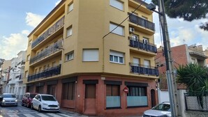 Un edificio amarillo de varios pisos con balcones, un paso de peatones y coches estacionados.