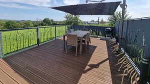 Une terrasse en bois avec une table et des chaises, un barbecue et une vue sur un champ verdoyant.
