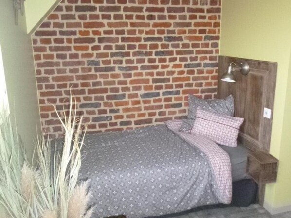 A room with a brick wall, a bed with a patterned bedspread, pillows, a nightstand, and a lamp.