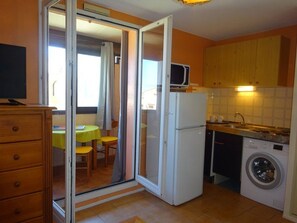 Eine kompakte Küche mit Kühlschrank, Mikrowelle, Waschmaschine und einer Essecke mit Tisch und Stühlen.