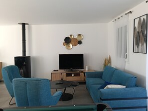 Ein Wohnzimmer mit Fernseher, zwei blauen Sofas, einem schwarzen Kamin und einem Wandbild.