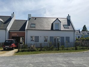Ein zweistöckiges Haus mit Garage, davor ein rotes Auto und ein Holzzaun.