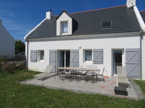 Ein weißes Gebäude mit grauem Dach, einem kleinen Balkon und einem Tisch mit Stühlen davor.