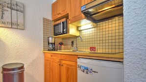 Een kleine keuken met houten kastjes, een magnetron, een koffiezetapparaat en een koelkast.