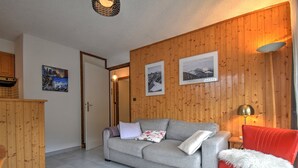 Een woonkamer met een grijze bank, een rode fauteuil, houten paneelwanden en een betegelde vloer.