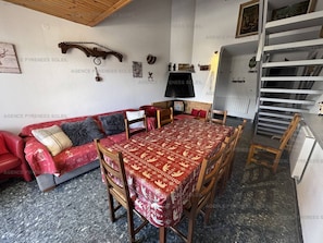 A cozy living room with a red sofa, a dining table with chairs, and a fireplace. - Ideal duplex apartment, village centre - 8 guests (Les Angles)