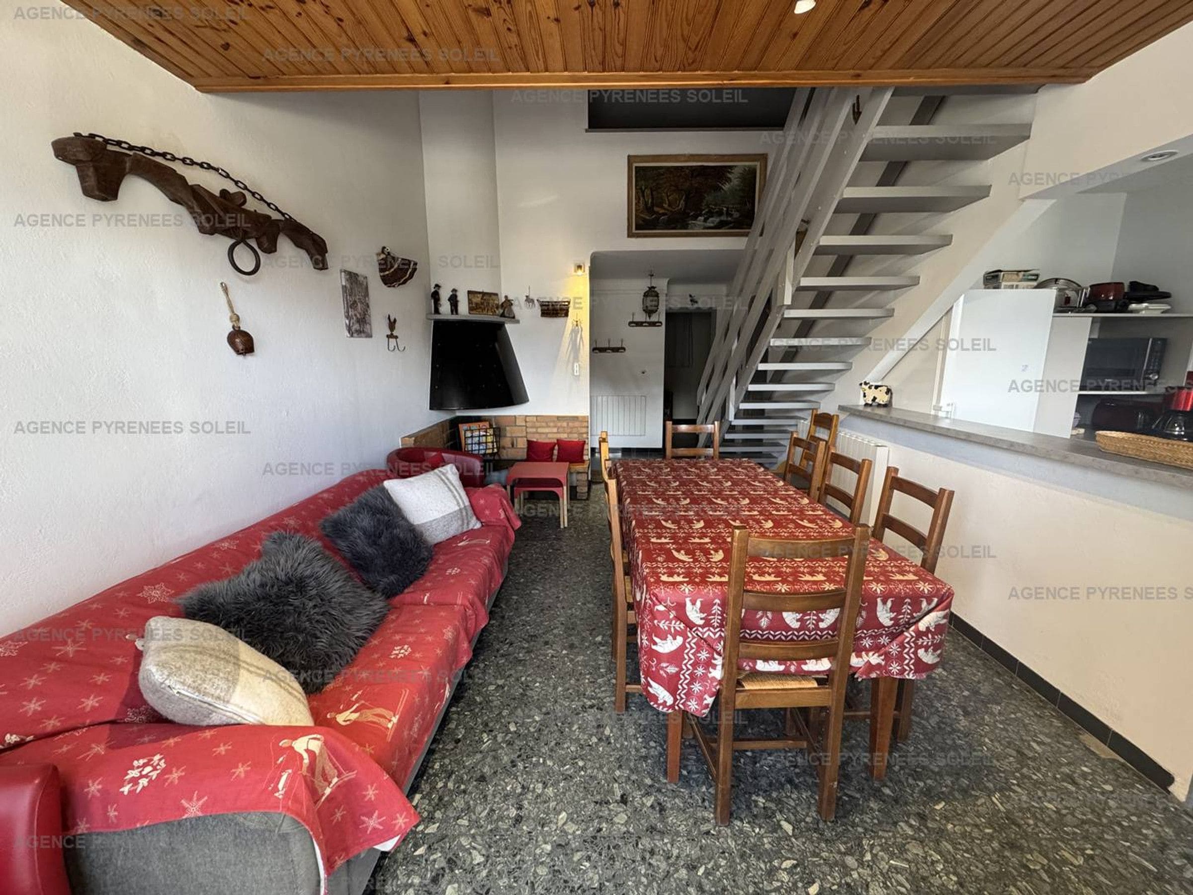 Een gezellige zithoek met een bank, eettafel en stoelen, een open haard en een trap naar een verdieping erboven.