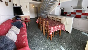 A cozy living area with a red sofa, a dining table with chairs, a kitchen with a red and white checkered backsplash, and a staircase. - Ideal duplex apartment, village centre - 8 guests (Les Angles)