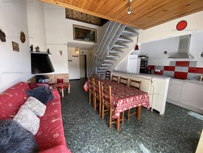 Ein gemütlicher Wohnbereich mit einem roten Sofa, einem Esstisch mit Stühlen, einer Küche mit rot-weißer Schachbrettfliese und einer Treppe.