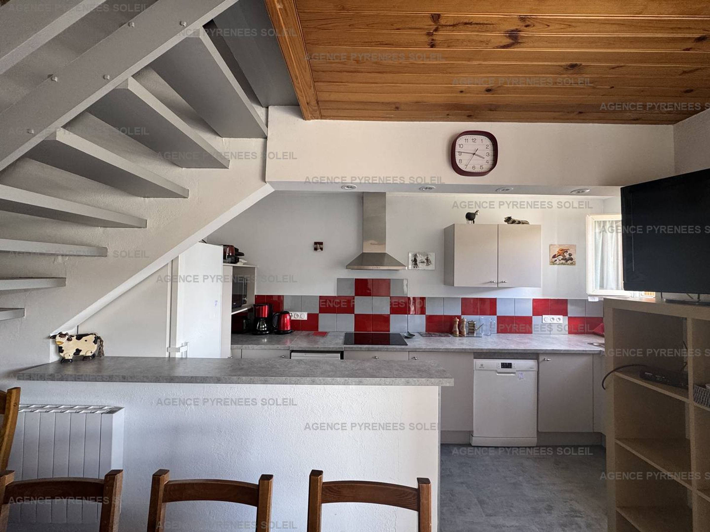 Eine moderne Küche mit einer zentralen Kochinsel, einem Essbereich mit Stühlen und einer Treppe, die zu einer weiteren Ebene führt.