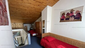A room with a wooden ceiling, a bed with a red blanket, a painting on the wall, and a bathroom visible through an open door. - Ideal duplex apartment, village centre - 8 guests (Les Angles)
