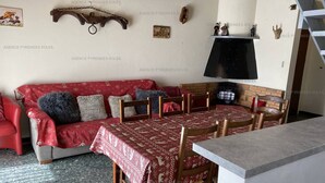 A cozy living room with a red sofa, wooden chairs, a dining table, and a fireplace. - Ideal duplex apartment, village centre - 8 guests (Les Angles)