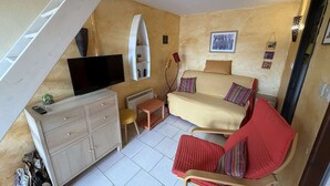 Ein kleines Zimmer mit einem Bett, einem Fernseher, einem kleinen Tisch, einem Stuhl und einem weißen Schrank.