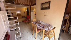 Ein kompakter Wohnraum mit Schlafgalerie, einem Esstisch mit Stühlen, einem roten Sessel, einer weißen Tür und einer Küchenzeile.