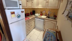 Eine kompakte Küche mit Kühlschrank, Mikrowelle, Geschirrspüler und Holzschränken.