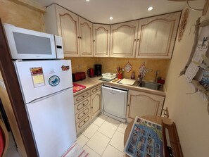 A compact kitchen with a refrigerator, microwave, dishwasher, and wooden cabinets. - Villa with pool and AC - 4 guests (La Franqui)