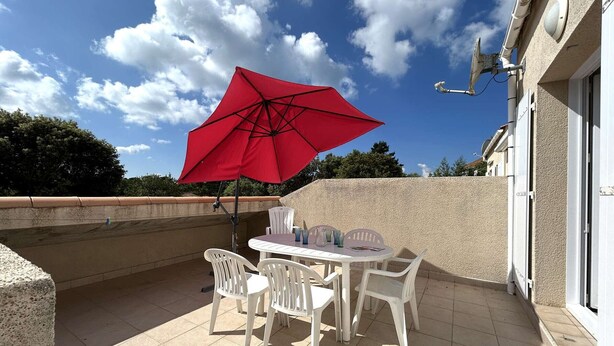 Een terras met een tafel en stoelen, een rode parasol en een gebouw op de achtergrond.
