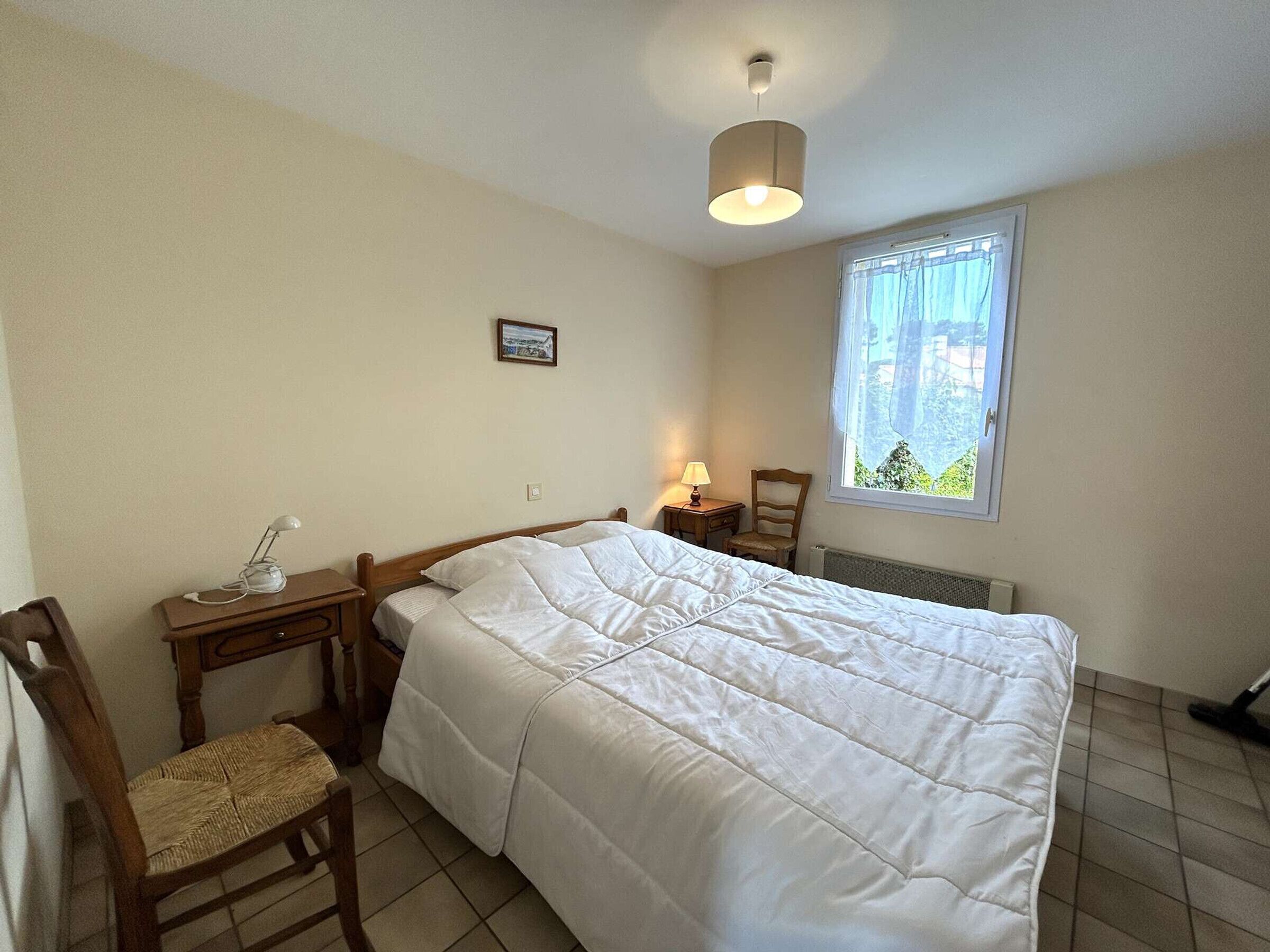 A bedroom with a bed, a chair, a desk, a lamp, a picture on the wall, and a window with a view.