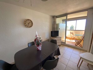 Ein Essbereich mit Tisch, Stühlen, einer Uhr, einem Fernseher auf einem Schrank und einem Balkon mit einer Schiebetür.