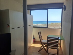 Ein Balkon mit Blick auf den Strand, einem Tisch, einem Stuhl und einem Kühlschrank.