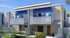 A modern two-story residential building with balconies, a small garden area, and a clear sky. - Two-story Townhouses a few Steps From the Beach (San Michele al Tagliamento)