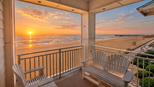 Un balcón con dos sillas Adirondack, vista a la playa y un muelle a lo lejos.