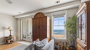 Una sala de estar con un sofá, un aparador de madera, una lámpara y vista al océano a través de amplias ventanas.