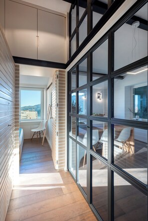 Ein modernes Interieur mit Holzboden, einem Essbereich mit weißen Stühlen und Blick durch große Fenster.