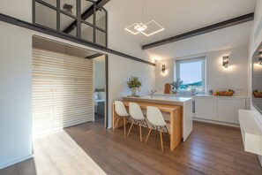 Eine moderne Küche mit einer Holztheke, weißen Stühlen und Blick ins Freie.