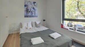 A bedroom with a bed, a window with a view of parked cars, a painting on the wall, and a chair. - Żeromskiego 23 by Grand Apartments (Gdynia)