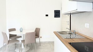 Een kleine keuken met een ronde eettafel, stoelen, een inbouwspoelbak en een wandairconditioner.