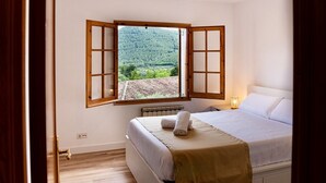 Ein Schlafzimmer mit Bett, einem Fenster mit geöffneten Rollläden, einer Heizung und Blick auf einen bewaldeten Bereich.